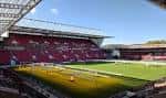 Vista interior del estadio Ashton Gate con gradas rojas y campo de césped bajo cielo azul