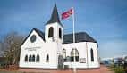 Fachada frontal de la iglesia noruega con bandera ondeando en un día soleado