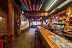 Interior del bar con bandera estadounidense en el techo y barra de madera