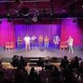 Grupo de comediantes actuando en el escenario bajo luces de colores