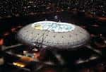 Vista aérea nocturna del Estadio Único Diego Armando Maradona con iluminación y público en las gradas
