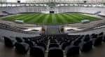 Interior del estadio mostrando cancha de césped y gradas vacías desde una perspectiva elevada