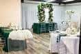 Interior del salón de eventos con mesas decoradas y arco floral verde