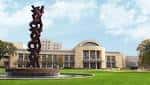 Vista exterior de la biblioteca con una escultura moderna en primer plano