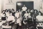 Sala de clases histórica con estudiantes y profesor frente a un pizarrón