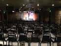 Interior del auditorio vacío con butacas negras y escenario iluminado
