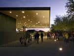 Fachada iluminada del museo al atardecer con visitantes caminando