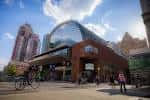 Plaza frontal del Kimmel Center con personas caminando y ciclistas bajo cielo parcialmente nublado