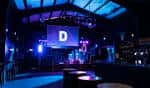 Interior del club District con escenario iluminado en azul y pantalla central