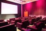 Sala de cine interior con butacas rojas y pantalla grande en ambiente oscuro