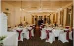 Sala de eventos decorada para una celebración con mesas redondas, sillas blancas y centros de mesa elegantes