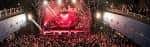 Interior del auditorio durante un concierto con escenario iluminado en rojo y público multitudinario