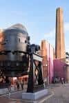 Plaza frontal del museo mostrando el gran horno de fundición y la chimenea bajo cielo despejado