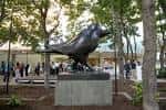 Escultura de pájaro en el parque rodeada de árboles y visitantes