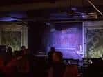 Escenario del club de comedia con luces de fondo y público sentado