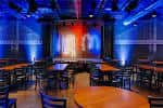 Interior del club de comedia con escenario iluminado y mesas dispuestas