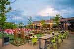 Terraza exterior de Chicken N Pickle con mesas y sillas coloridas bajo el cielo al atardecer