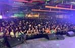 Concierto en vivo con banda tocando frente a una multitud animada bajo luces de escenario