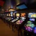 Largo pasillo con múltiples máquinas recreativas y luces de neón en el Quarters Arcade Bar