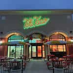 Fachada exterior de Tiki Taco con letrero neón verde y mesas al aire libre