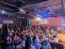 Interior del Upstage Comedy Lounge con público sentado en mesas durante una función de comedia