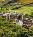 Vista panorámica del palacio desde una colina verde con paisaje escocés