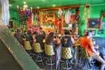 Bar con ambiente vibrante, clientes sentados en taburetes y decoración colorida