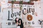 Pareja posando frente al letrero de Love City Brewing en una boda