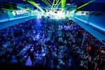 Interior del salón principal durante un evento nocturno con iluminación láser y público asistiendo
