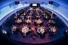 Configuración circular de mesas para banquete en el interior del venue con iluminación ambiental azul