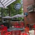 Área al aire libre de Hudson Grille Midtown con mobiliario rojo y letrero circular
