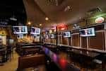 Zona interior de Hudson Grille con asientos altos y televisores colgantes