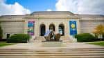Fachada principal clásica del museo con escalinata, escultura y banderines de exhibición