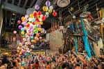 Gran sala de eventos con globos multicolores y multitud de asistentes