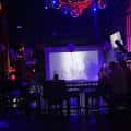 Escenario interior con pantalla proyectada y luces azules durante un evento