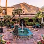 Mujer junto a fuente decorativa en patio con montañas al fondo