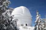 Domo del observatorio cubierto de nieve entre árboles invernales