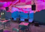 Interior del local con mesas y decoración colorida bajo luces rosas