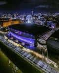 Fotografía aérea nocturna de la arena iluminada con luces azules y púrpuras junto al río