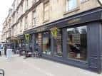 Fachada exterior del bar Dram! en Glasgow con escaparate y mesas al aire libre