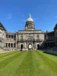 Vista frontal del edificio principal de la Universidad de Edimburgo con su cúpula característica y césped verde