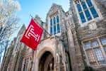 Fachada histórica de piedra con bandera roja de Temple University en primer plano