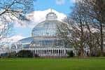 Vista frontal del Palm House de Sefton Park con césped verde y árboles en primer plano