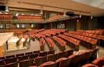 Interior del auditorio principal con butacas rojas dispuestas en gradas y escenario amplio