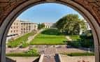 Vista del campus universitario a través de un arco de piedra con césped y edificios al fondo