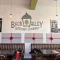 Interior del bar con el logo de Back Alley Brewing en la pared y mesas para eventos