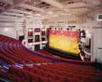 Interior del teatro mostrando el escenario con cortina amarilla y plateas curvas