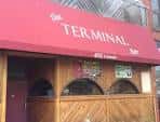 Fachada exterior de The Terminal Bar con toldo rojo y letrero visible