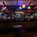 Interior del bar con barra iluminada, luces de neón y ambiente festivo