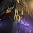 Fachada nocturna del club Massive con letrero iluminado y banderas